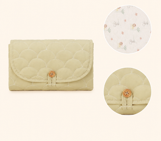 Foldable baby changing mat in a quilted beige clutch with soft printed lining and button closure.