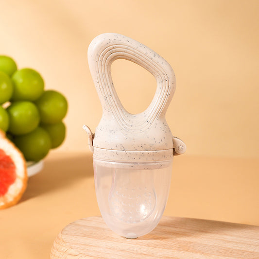 A silicone baby fruit feeder with a soft textured handle and clear feeding chamber, displayed on a warm peach background with fresh fruit.